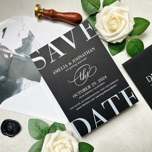 May include: Black and white save the date card with a photo of a couple on the front. The card says "Save the Date" in large white letters and "Amelia & Johnathan are getting married!" in smaller white letters. The date is October 29, 2024 and the location is Palm Springs, California. The card also includes a website address for more information.