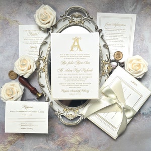May include: A white wedding invitation with gold lettering. The invitation features a large gold letter "A" with ornate details. The text reads "Mr. & Mrs. David Clark Olson request the honor of your presence at the marriage of their daughter Miss Julia Marie Olson to Mr. Adam Raid Richards son of Mr. & Mrs. Gregory Martin Richards Saturday, the fifth of November two thousand and twenty two at five in the evening Ashton Gardens, North Houston 1315 Interstate Forest Boulevard Houston, Texas Reception Immediately Following Formal Attire"
