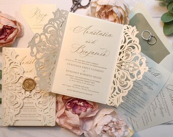 May include: A white and gold wedding invitation with a laser-cut design. The invitation reads "Anastasia and Benjamin" and includes the wedding date and location.