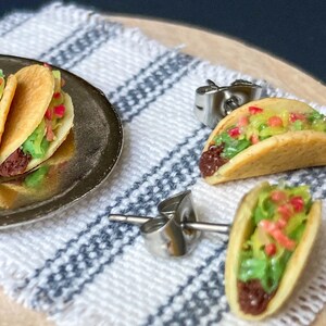 Peut inclure: Une paire de boucles d'oreilles &agrave; clous argent&eacute;es avec des tacos miniatures. Les tacos sont faits en p&acirc;te polym&egrave;re et pr&eacute;sentent une garniture brune, de la laitue verte et des garnitures rouges et jaunes.