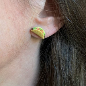 Peut inclure: Une paire de petites boucles d'oreilles en forme de taco r&eacute;alistes. Les boucles d'oreilles sont en p&acirc;te polym&egrave;re et peintes pour ressembler &agrave; un taco avec de la laitue, de la tomate et du fromage.
