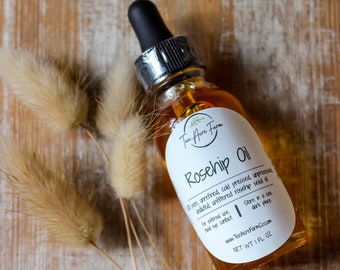May include: A clear glass bottle with a dropper filled with rosehip oil. The bottle has a white label with the text "Ten Acre Farm Rosehip Oil 1 fl oz. unrefined, cold pressed, unprocessed, undiluted, unfiltered rosehip seed oil. For external use. Avoid eye contact. Store in a cool dark place. www.TenAcreFarmCo.com NET WT 1 FL OZ"