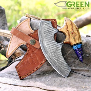 May include: A Damascus steel cleaver with a wooden handle and a leather sheath. The handle has a blue and purple inlay. The cleaver is a kitchen tool used for chopping and slicing.