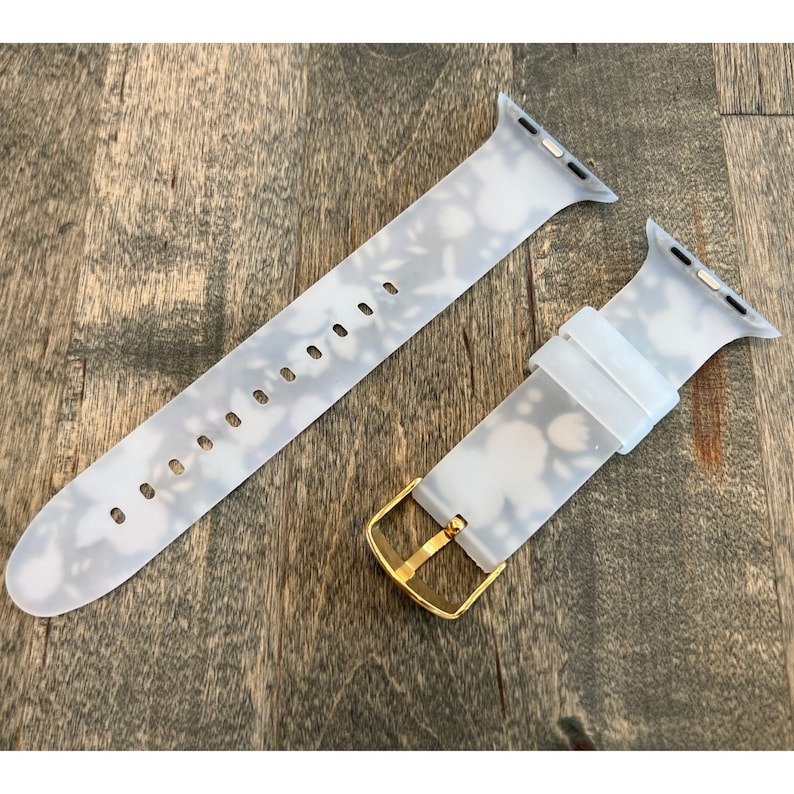 May include: A white silicone Apple Watch band with a floral pattern and a gold buckle.