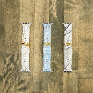 May include: Three Apple Watch bands with a marble pattern. The bands are white, blue, and gray with gold accents.