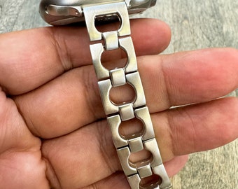 May include: A silver metal watch band with a unique link design. The band is made of a series of interlocking oval and rectangular links.