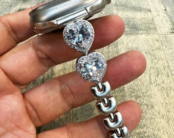 May include: Silver watch band with two heart-shaped charms encrusted with clear cubic zirconia stones.