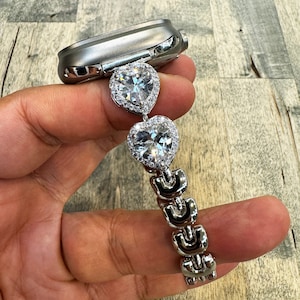 May include: A silver watch band with two large heart-shaped rhinestones. The band is made of metal links and has a silver finish.