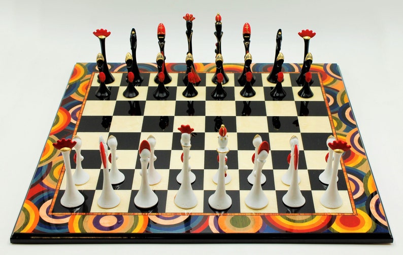 Pu&ograve; includere: Una scacchiera bianca e nera con un bordo circolare colorato. I pezzi degli scacchi sono bianchi e neri con accenti rossi e dorati. I pezzi sono disposti nelle loro posizioni di partenza.