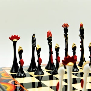 Pu&ograve; includere: Un set di scacchi bianco e nero con accenti rossi e dorati. I pezzi sono disposti su una scacchiera con un design astratto colorato.