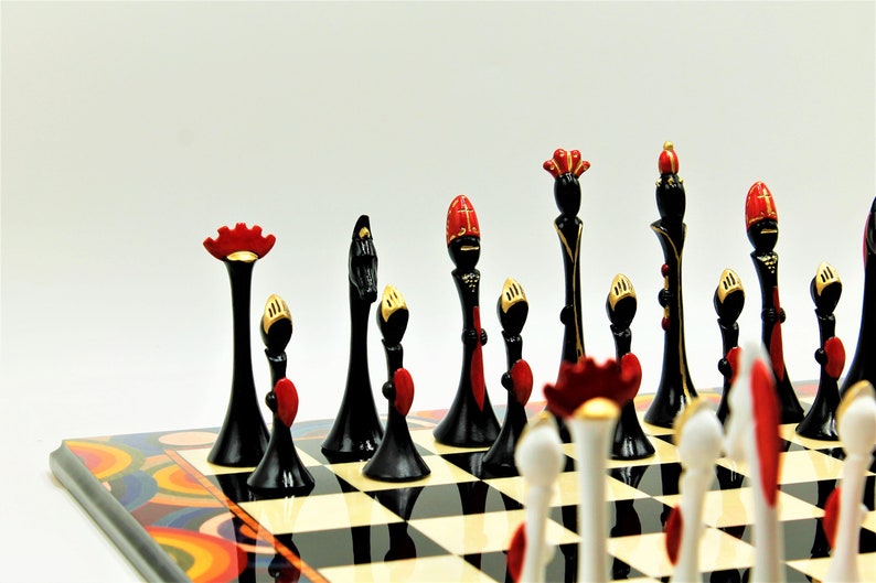 Pu&ograve; includere: Un set di scacchi bianco e nero con accenti rossi e dorati. I pezzi sono disposti su una scacchiera con un design astratto colorato.
