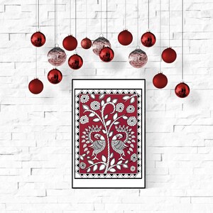May include: A framed print of a red background with a white design of two peacocks and a tree. The print is surrounded by a black frame and hanging on a white brick wall. Red Christmas ornaments are hanging from the ceiling above the print.