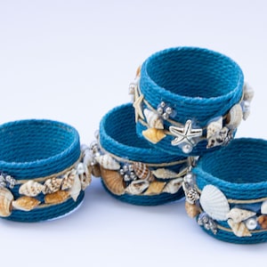 May include: Four blue rope napkin rings decorated with seashells and starfish. The rings are stacked on top of each other.