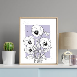 May include: A black and white line drawing of a bouquet of pansies on a light purple background. The drawing is framed in a light wood frame and is displayed on a shelf with a cactus and a lamp.