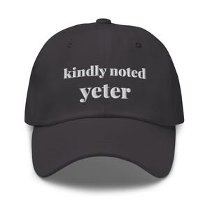 Könnte beinhalten: Eine schwarze Baseballkappe mit weißem, gesticktem Text auf der Vorderseite, der kindly noted yeter lautet. Die Kappe hat eine strukturierte Krone, einen gebogenen Schirm und einen Knopf oben, bestehend aus sechs Paneelen und Ösen.