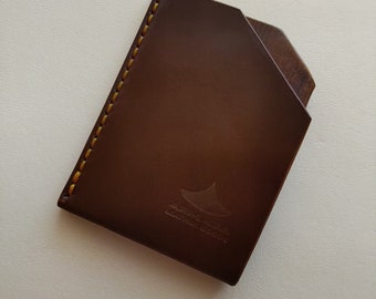 May include: A brown leather wallet with yellow stitching and a logo embossed on the front. The logo is a stylized image of a manta ray with the text "Manta Ray Leather" underneath.
