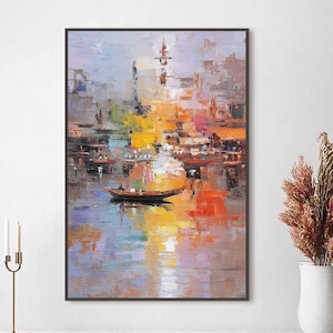 May include: An abstract oil painting of a waterfront scene with boats and buildings. The artwork features a vibrant palette of colors, including orange, yellow, blue, and red, with reflections in the water. The painting is framed in a black border.