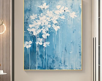 May include: Abstract floral painting with white flowers and dripping paint on a light blue background. The artwork is framed in a gold-colored frame. The painting is a modern piece of wall decor.