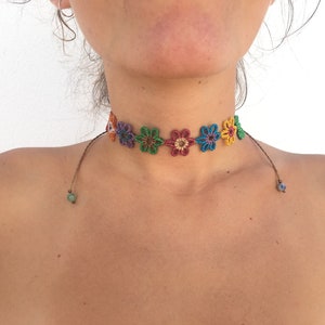 May include: A colorful crocheted flower choker necklace with green and blue beads on the ends of the cords.