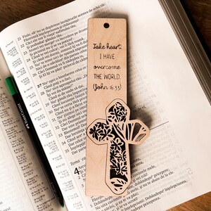 May include: A wooden bookmark with a floral cross design. The bookmark has the text "Take heart. I have overcome the world. (John 16:33)" on it.