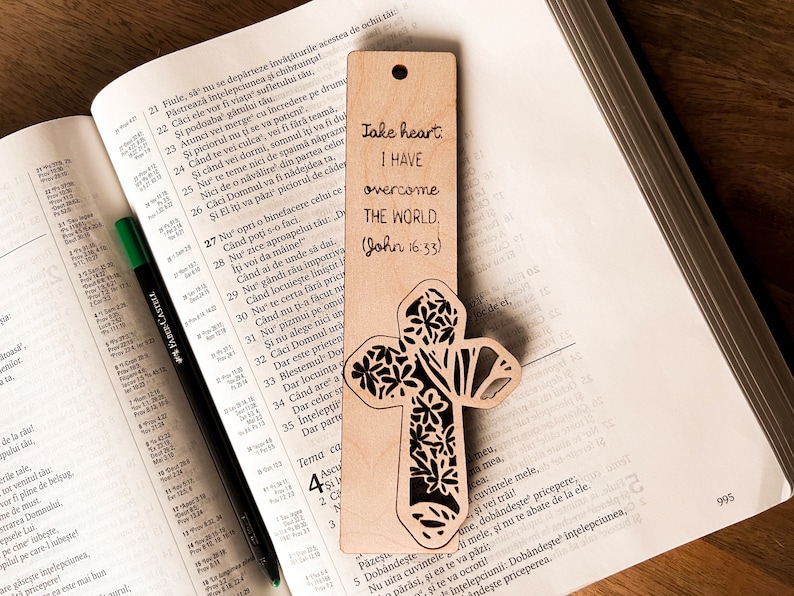 May include: A wooden bookmark with a floral cross design. The bookmark has the text "Take heart. I have overcome the world. (John 16:33)" on it.