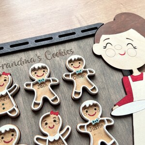 K&ouml;nnte beinhalten: Holzschild mit dem Text "Grandma's Cookies" und einer Ausschneidung einer Frau, die einen Teller h&auml;lt. Es gibt auch Ausschnitte von Lebkuchenm&auml;nnern mit Namen wie "Jack", "Oliver" und "Justin".