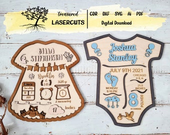 May include: Two wooden baby announcement signs, one shaped like a onesie and the other like a dress. The onesie sign is blue and says "Joshua Stanley" with birth details. The dress sign is pink and says "Bima Stiphinson" with birth details.