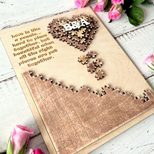 May include: A wooden heart-shaped puzzle with the letters "B&A" in the center. The puzzle is surrounded by a quote about love being like a puzzle. The quote reads: "Love is like a puzzle... hard to piece together, but beautiful when all the right pieces are put together."