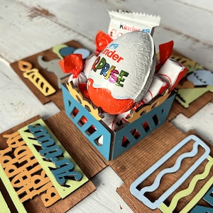 May include: A wooden box with a blue and yellow design. The box is open and filled with chocolate candies, including a Kinder Surprise egg. The box has a Happy Birthday message on the front.