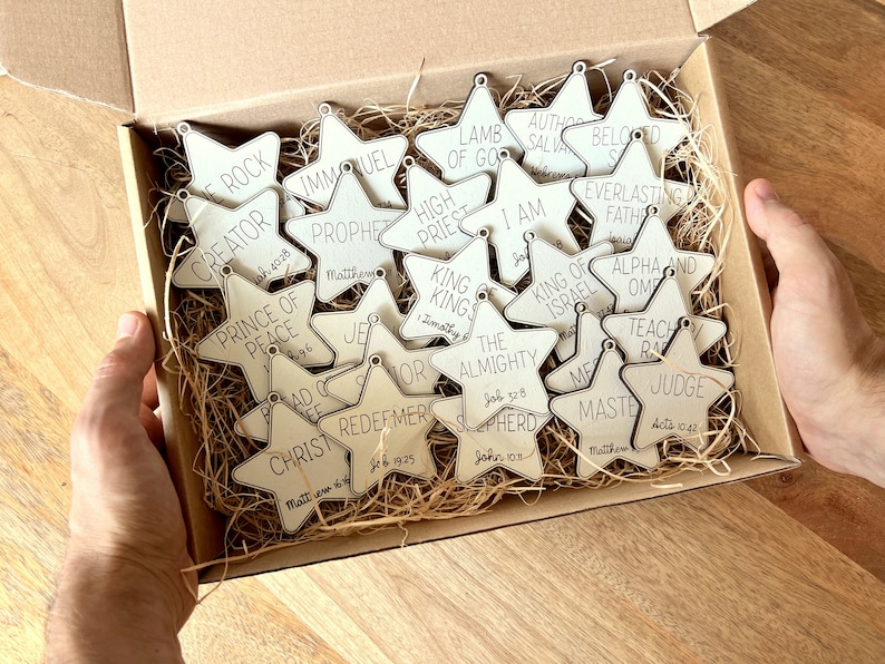 May include: A box filled with wooden star ornaments, each with a different biblical title and scripture reference. The titles include "Creator", "Prince of Peace", "Immanuel", "Prophet", "High Priest", "King of Kings", "The Almighty", "Shepherd", "Author and Savior", "Beloved", "Everlasting Father", "King of Israel", "Alpha and Omega", "Teacher", "Master", and "Judge".