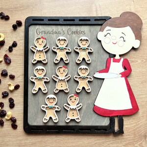 K&ouml;nnte beinhalten: Ein Holz-Lebkuchen-Backset mit einer Frau, die einen Teller h&auml;lt. Das Set enth&auml;lt acht Lebkuchen mit Namen wie "Oliver", "Sarah" und "Jack". Das Set ist mit "Grandma's Cookies" beschriftet.