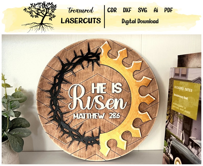 May include: A round wooden sign with a brown background and a chevron pattern. The sign features a black crown of thorns, a gold gear, and white text that reads "He is Risen Matthew 28:6".