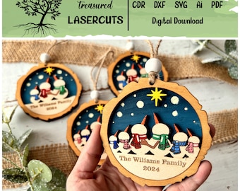May include: Set of four wooden Christmas ornaments featuring a family of snowmen with scarves and hats. The ornaments are decorated with a blue background, white snowflakes, and a yellow star. The text "The Williams Family 2024" is inscribed on the bottom of each ornament.