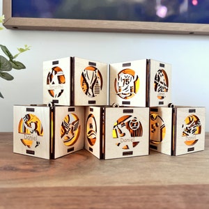 May include: Eight wooden candle holders with different sports-themed designs. Each holder has a name on it, including Samantha, James, and Daniel.
