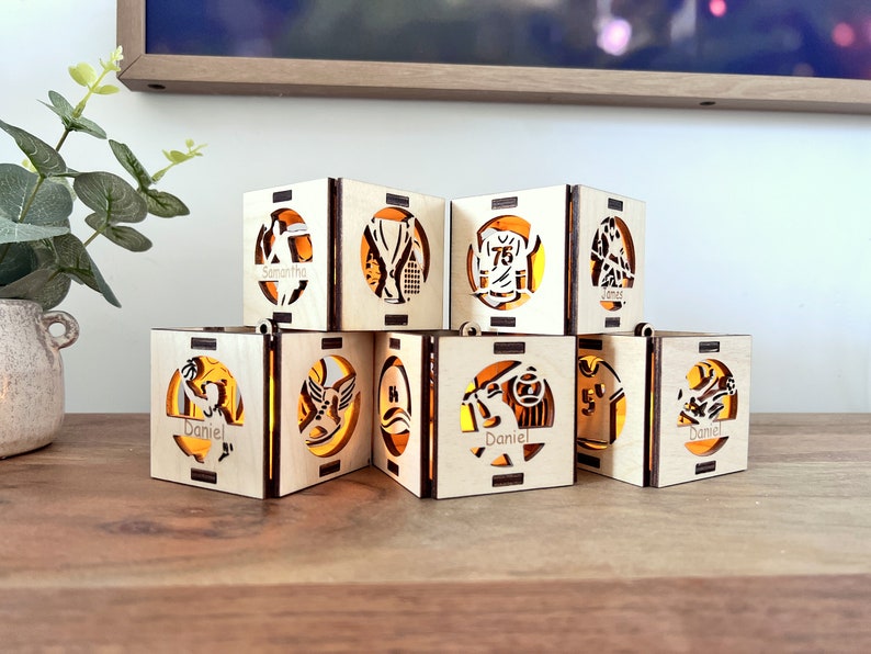 May include: Eight wooden candle holders with different sports-themed designs. Each holder has a name on it, including Samantha, James, and Daniel.