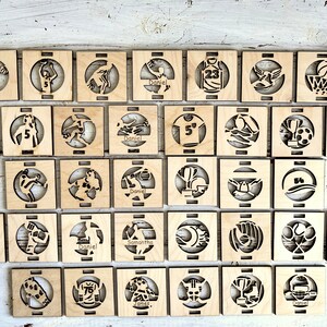 May include: A collection of 36 wooden coasters with various sports-themed designs. Each coaster features a different sport, including basketball, soccer, baseball, and football. The coasters are personalized with names like "Daniel", "Samantha", and "James".