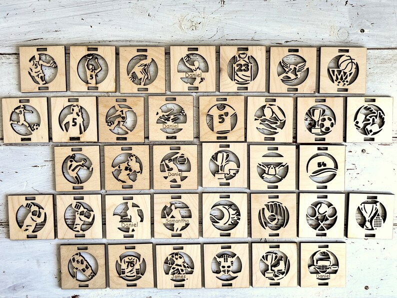 May include: A collection of 36 wooden coasters with various sports-themed designs. Each coaster features a different sport, including basketball, soccer, baseball, and football. The coasters are personalized with names like "Daniel", "Samantha", and "James".