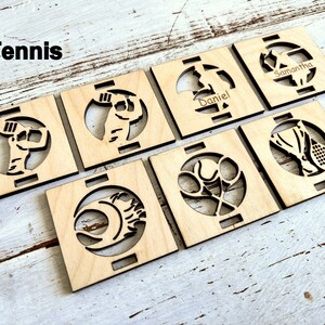 May include: Set of seven wooden coasters with a tennis theme. Each coaster features a different tennis-related design, including a tennis player, a tennis racket, and a tennis ball. The coasters are personalized with the names "Samantha" and "Daniel".