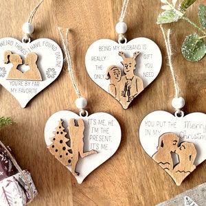 May include: Four wooden heart-shaped ornaments with different sayings and illustrations. The ornaments are white with brown wood accents. The sayings include "Of all the weird things I have found online, you're by far my favorite", "Being my husband is really the only gift you need", "It's me. Hi. I'm the present. It's me." and "You put the Merry Christmas in my".
