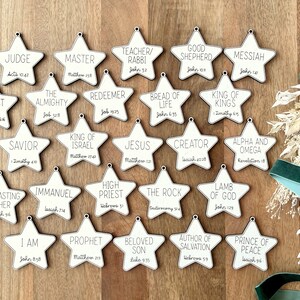 May include: Twenty white wooden star ornaments with black text. Each star features a different name or title for Jesus, along with a corresponding Bible verse.