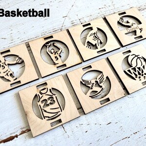 May include: Six wooden coasters with laser-cut designs featuring basketball-themed images, including a basketball player, a basketball hoop, and a basketball shoe. The coasters are unfinished and ready to be painted or stained.