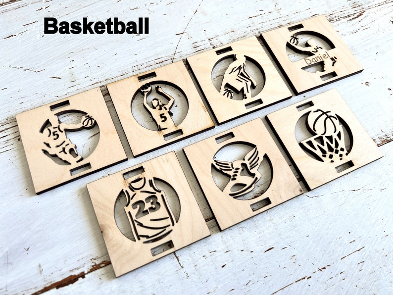 May include: Six wooden coasters with laser-cut designs featuring basketball-themed images, including a basketball player, a basketball hoop, and a basketball shoe. The coasters are unfinished and ready to be painted or stained.