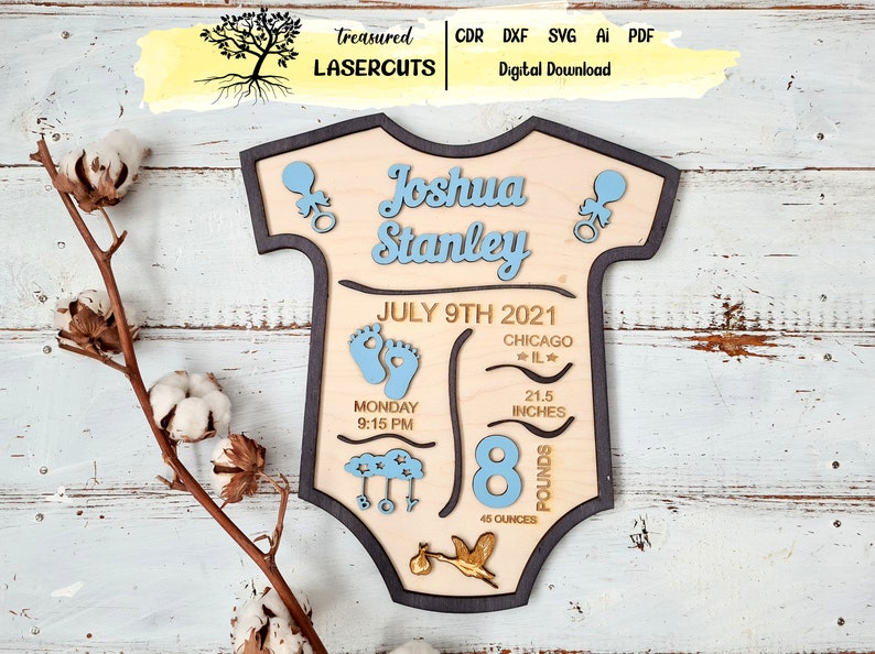 May include: A wooden baby onesie-shaped sign with the name Joshua Stanley, birth date July 9th, 2021, time of birth 9:15 PM, location Chicago, IL, weight 8 pounds, 45 ounces, and length 21.5 inches. The sign is decorated with blue and gold accents.
