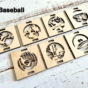 May include: Set of six wooden baseball-themed coasters with various designs, including a baseball glove, a baseball player, a baseball cap, and a baseball bat. The coasters are made of natural wood and have a light brown color.