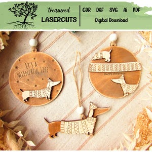 May include: Wooden dachshund ornaments with etched details. One ornament reads "It's a Wienerful Life" and another says "merry christmas". The dachshunds are wearing sweaters and hats. The ornaments are hanging from twine.
