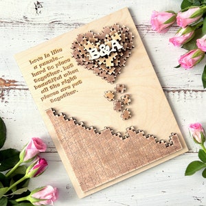 May include: A wooden heart-shaped puzzle with the letters "B&A" in the center. The puzzle is surrounded by a quote about love being like a puzzle. The quote reads: "Love is like a puzzle... hard to piece together, but beautiful when all the right pieces are put together."