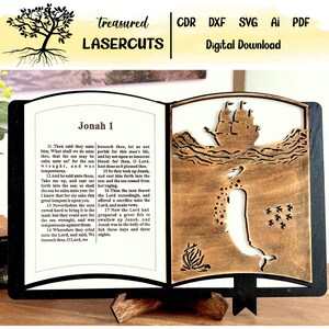 Puede incluir: Un recorte de madera con forma de libro que representa una escena de la historia bíblica de Jonás y la ballena. El lado izquierdo del recorte presenta una página del libro de Jonás, con el texto "Jonás 1" y los versículos 11-17. El lado derecho del recorte presenta una ballena tragando a Jonás, un barco en el agua y algunas estrellas. El recorte está sobre un soporte de madera.