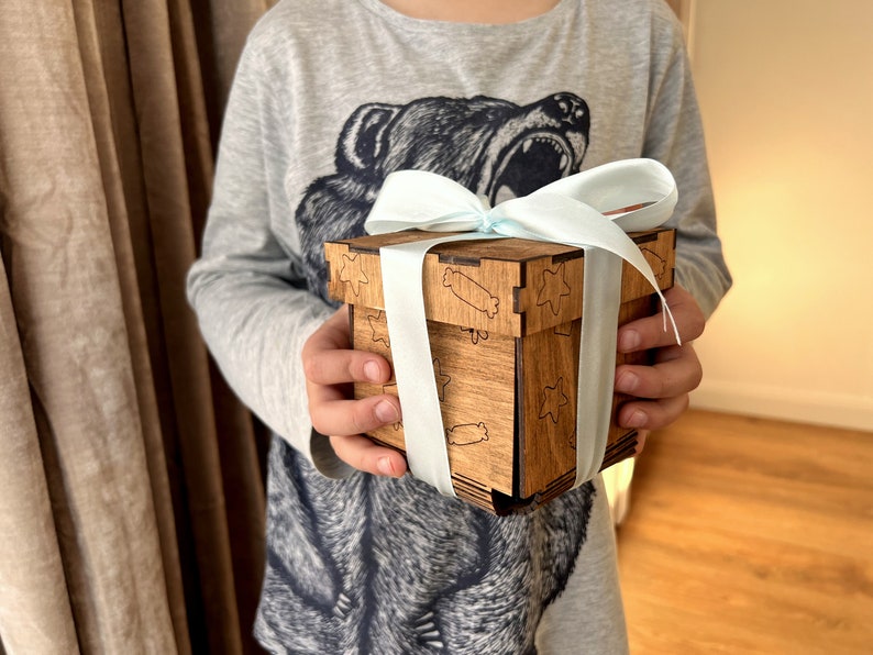 May include: A wooden box with a light blue ribbon tied around it. The box has a star and candy cane design engraved on it.
