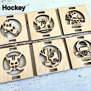 May include: Six wooden squares with laser cut designs of hockey equipment and the names "James" and "Daniel".