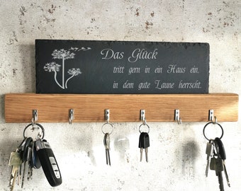 May include: A wooden key rack with five hooks and a black slate sign that reads "Das Glück tritt gern in ein Haus ein, in dem gute Laune herrscht."